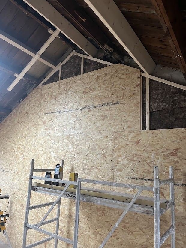 Attic wall being insulated and clad with OSB boards, with scaffolding in the room