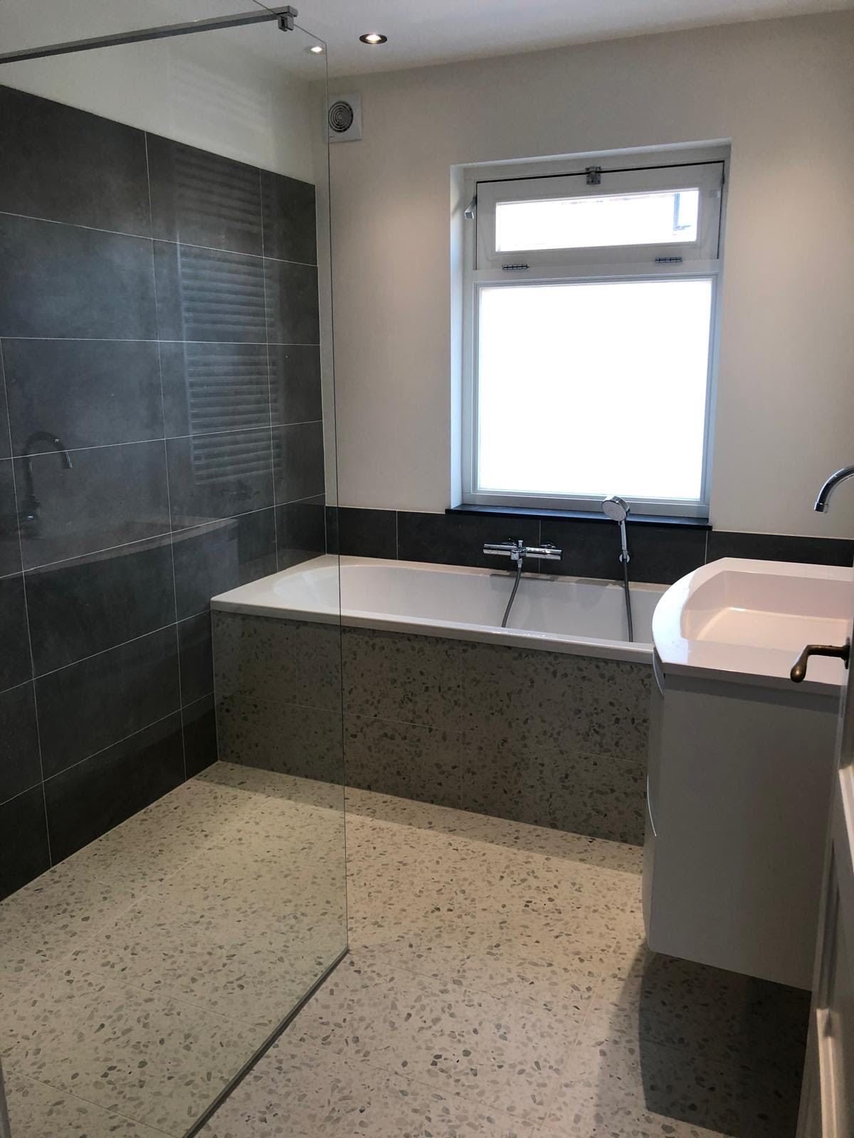 Bathroom with dark grey wall tiles, built-in bath, terrazzo-look floor and white vanity unit
