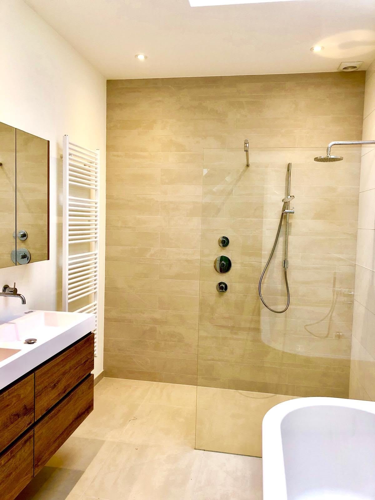 Bathroom with walk-in rain shower, large beige wall tiles, wooden vanity unit and freestanding bath
