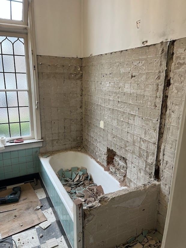 Old bathroom being stripped out, with tiles removed and the bath still in place