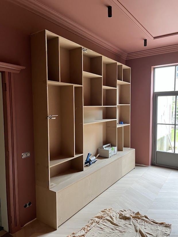 Built-in TV and bookcase wall in a room with high ceilings and a pink wall