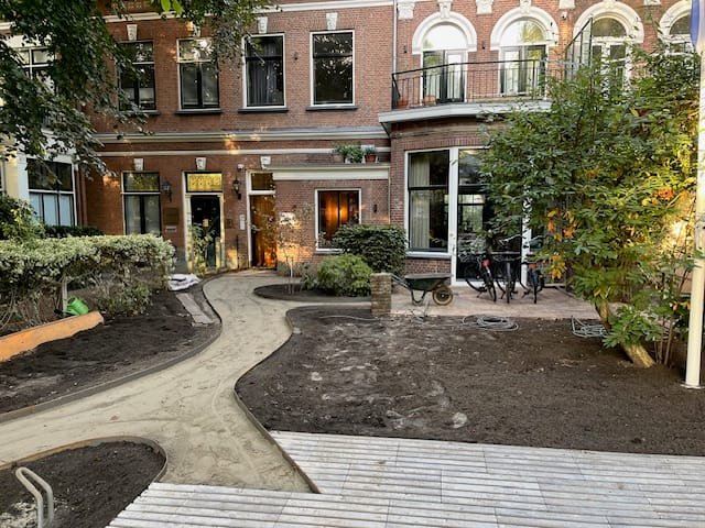Courtyard garden behind period brick homes with a curved sand path, steel-edged beds of fresh soil and a wooden deck