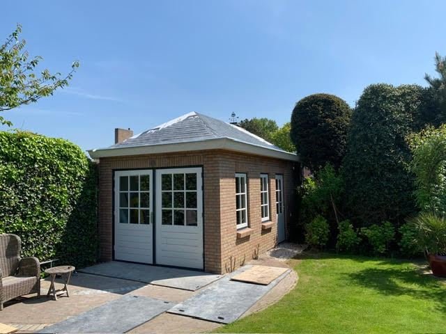 Finished brick garden building with hipped roof, white double doors and windows in a green garden