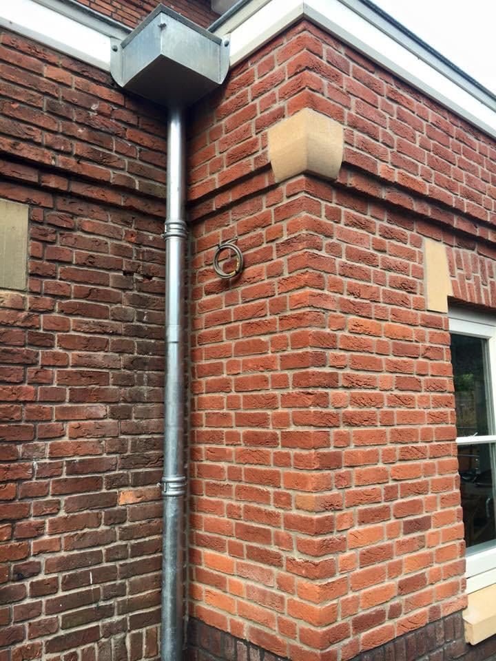 Zinc gutter box and downpipe on the corner of a brick house with stone details
