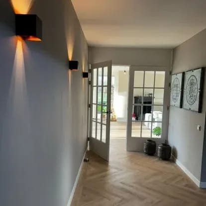 Hallway with black wall lights casting light up and down, glass doors and a herringbone floor