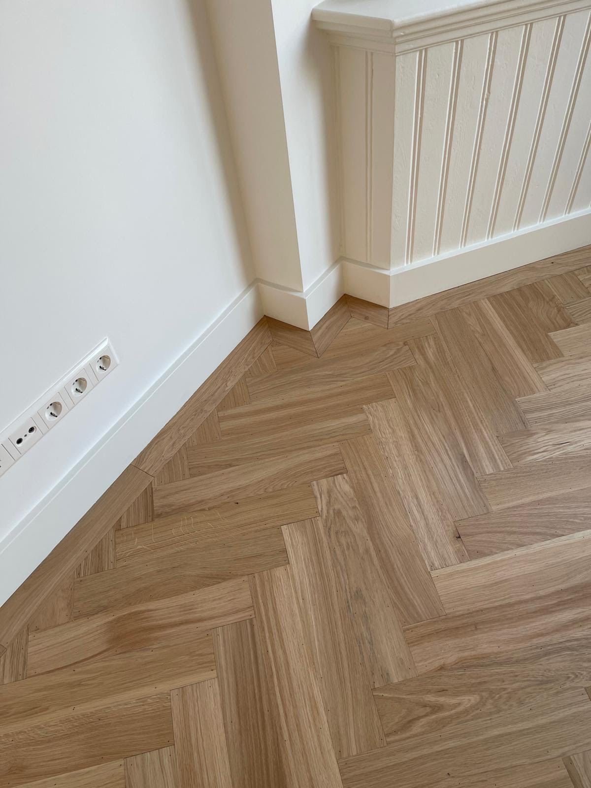 Detail of a new oak herringbone floor with white skirting and panelled wall cladding