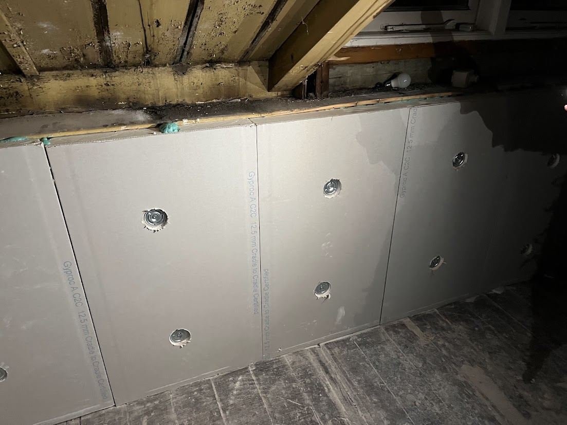 Insulation boards fixed to a wall with plugs, below a timber floor structure