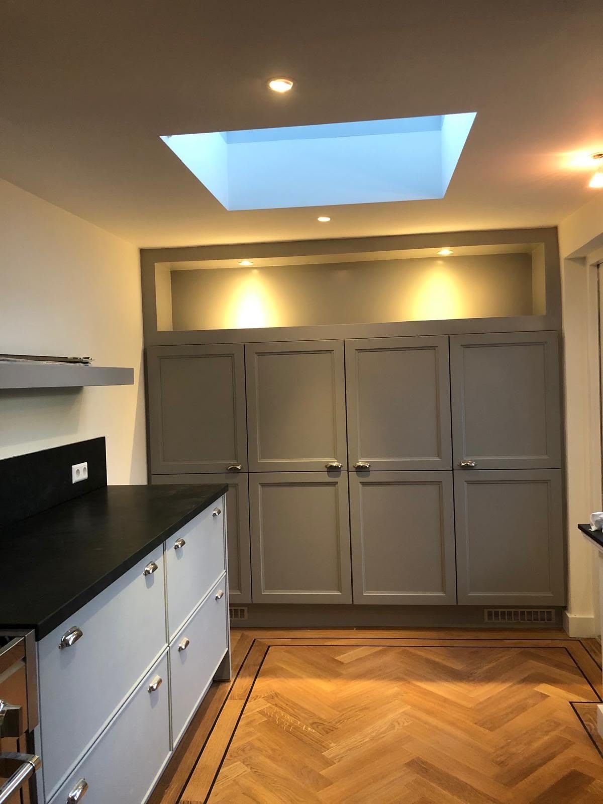 Kitchen with grey panelled cabinets, black worktop, rooflight and herringbone floor