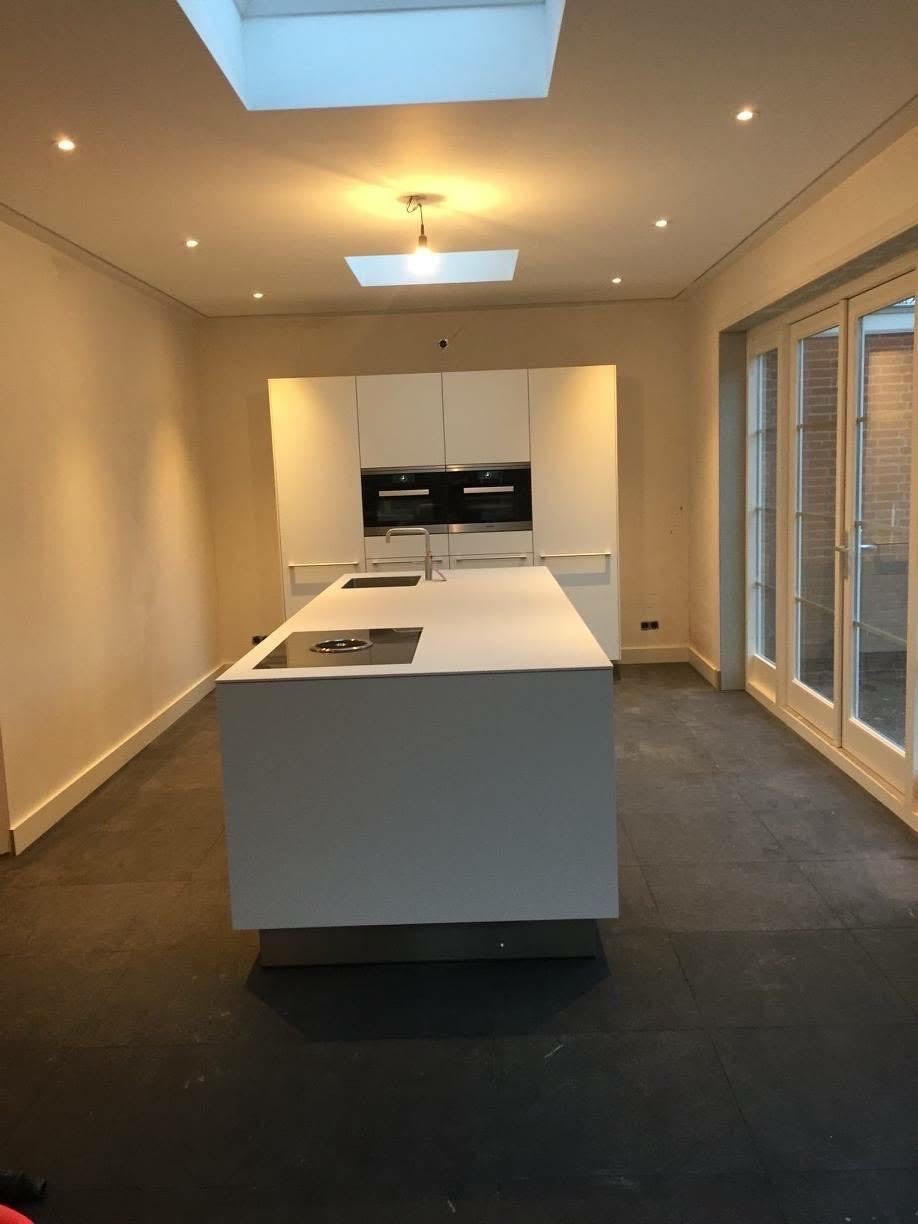 White kitchen with island and built-in ovens under a large rooflight and recessed spots