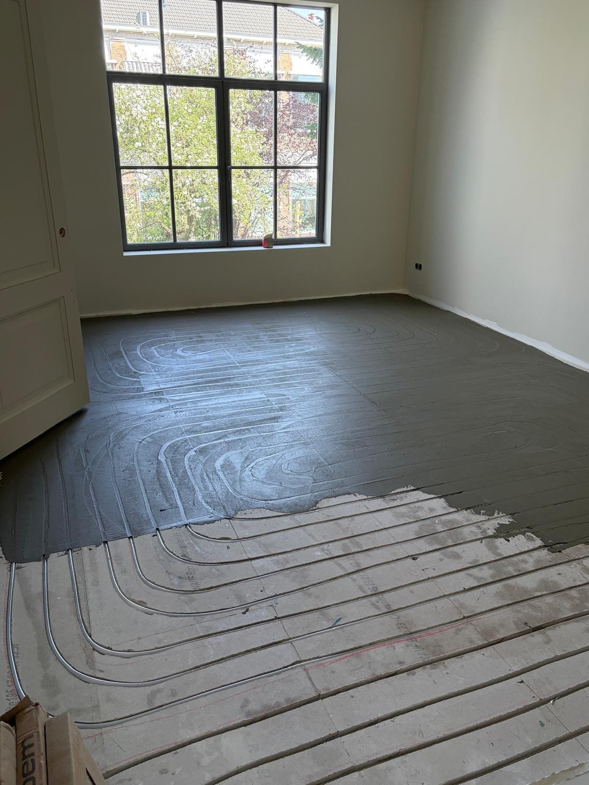 Underfloor heating pipes milled into an existing floor in an empty room with a large window