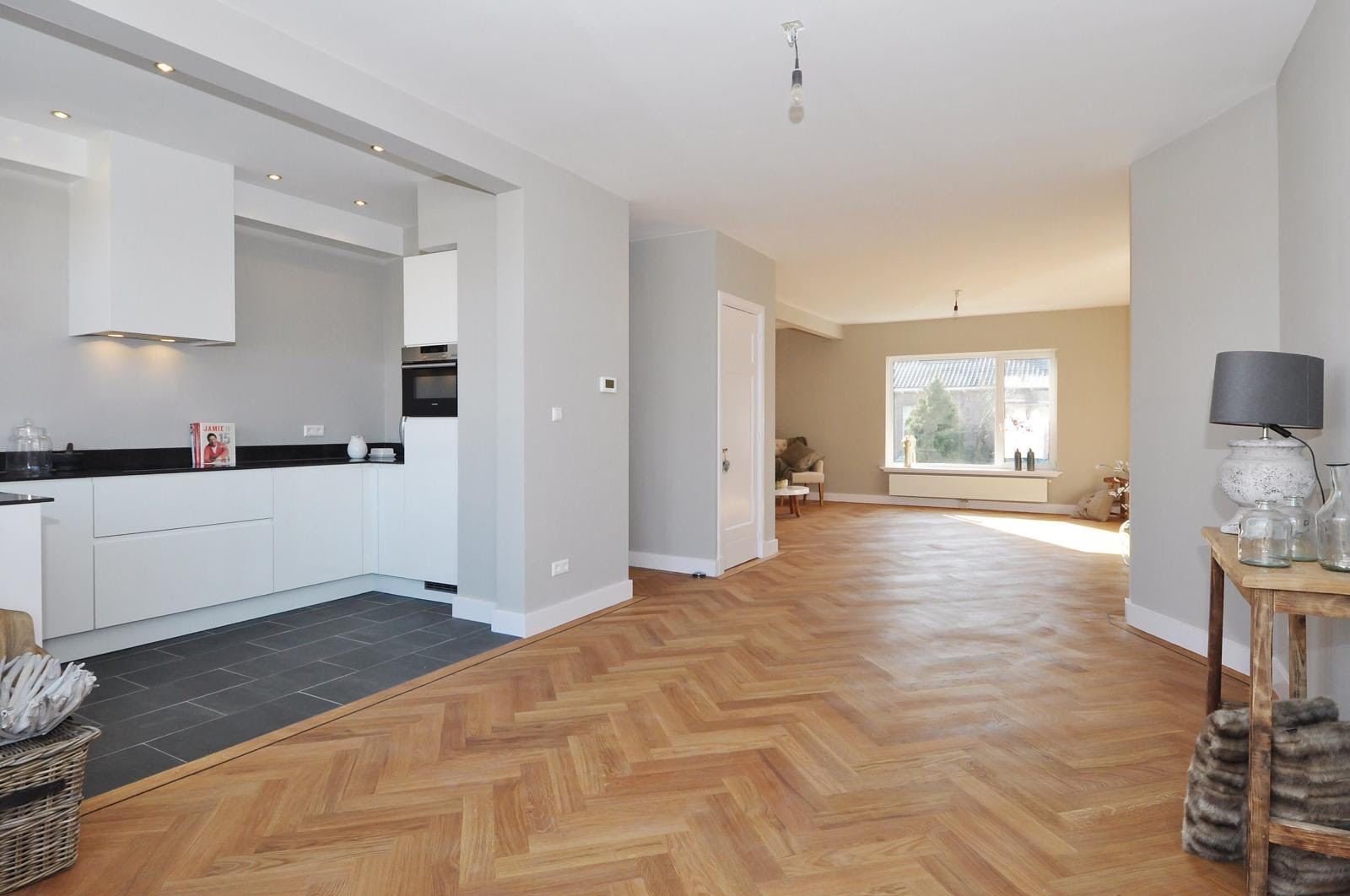 Open-plan white kitchen flowing into a living room with herringbone floor