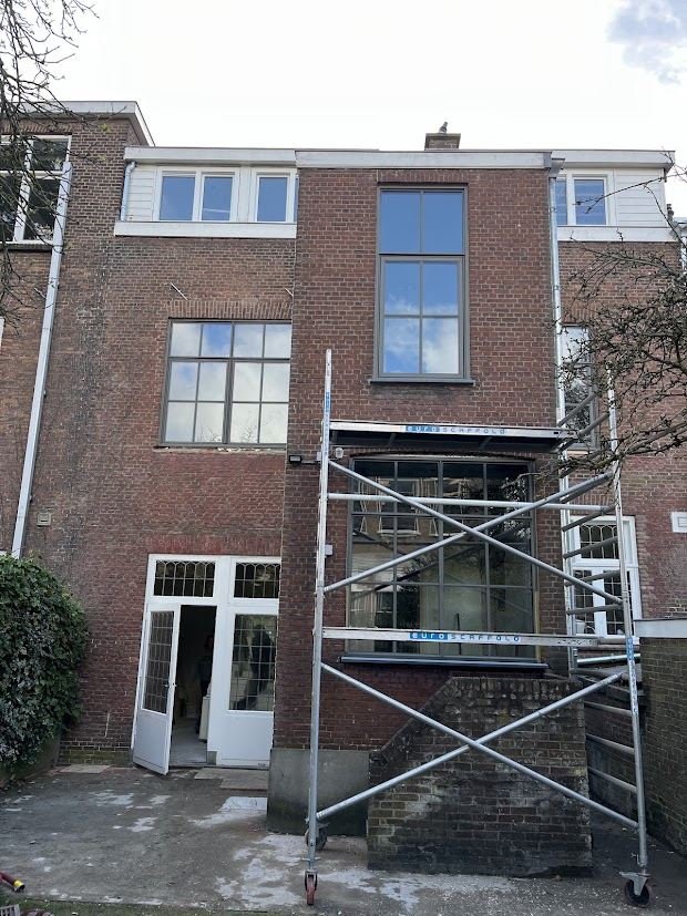 Rear facade of a three-storey brick terraced house with new white frames and garden doors, scaffolding on the side