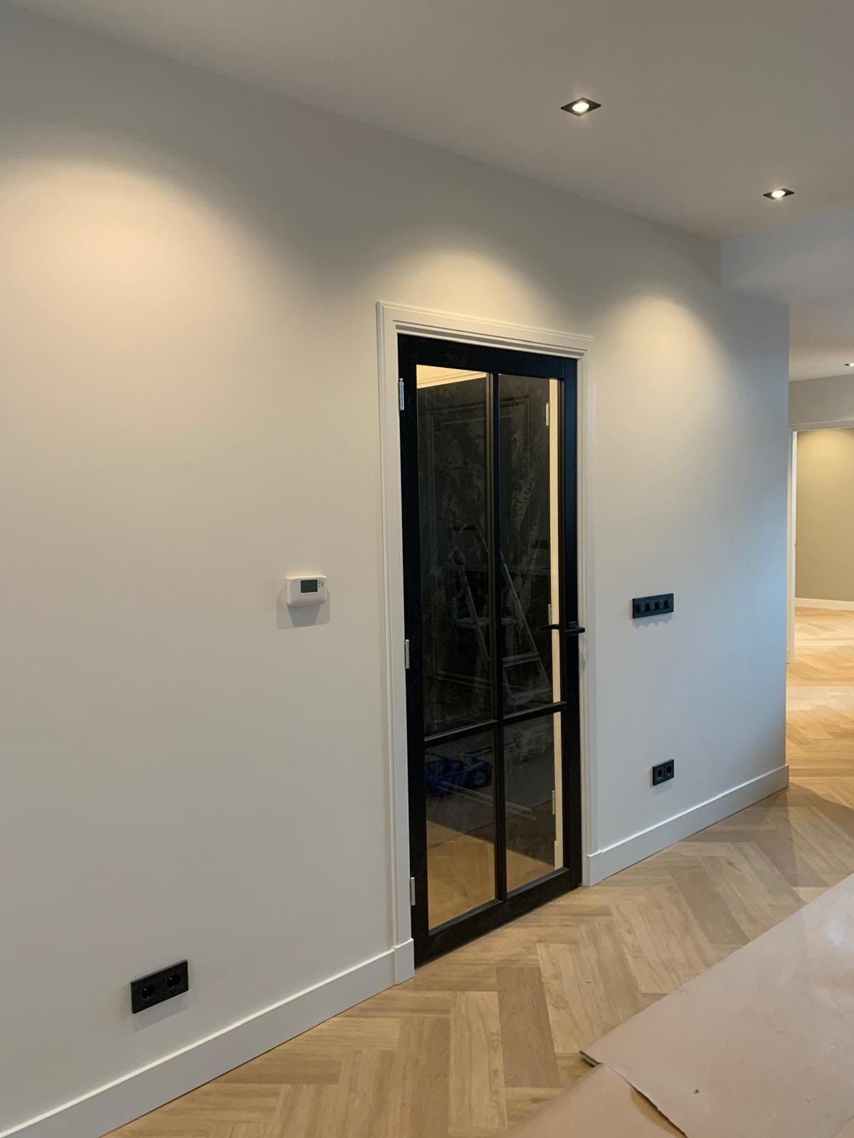Finished hallway with recessed ceiling spots, light walls and a black steel-framed door
