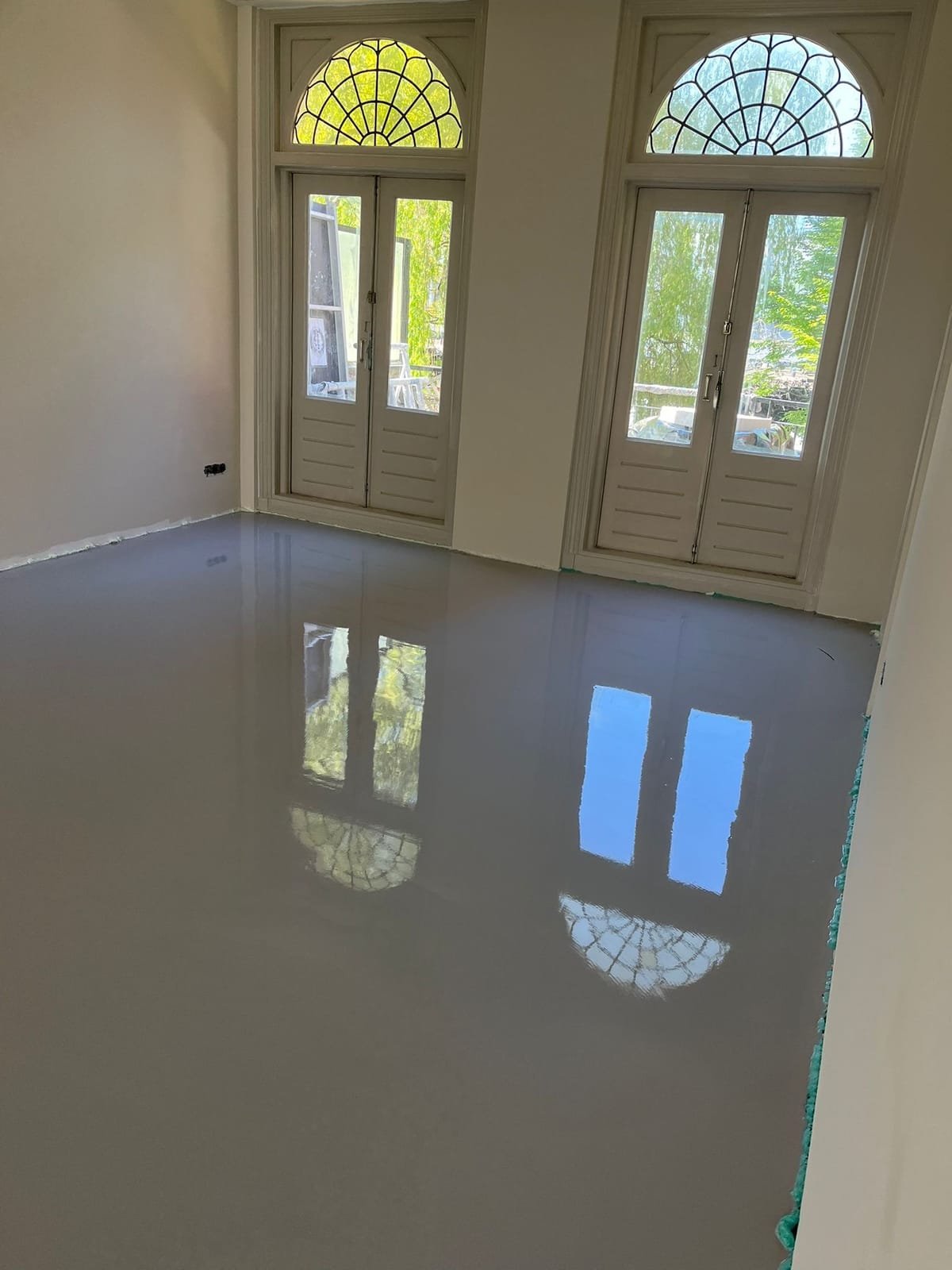 Freshly poured smooth screed in a period room with arched stained-glass windows above the doors