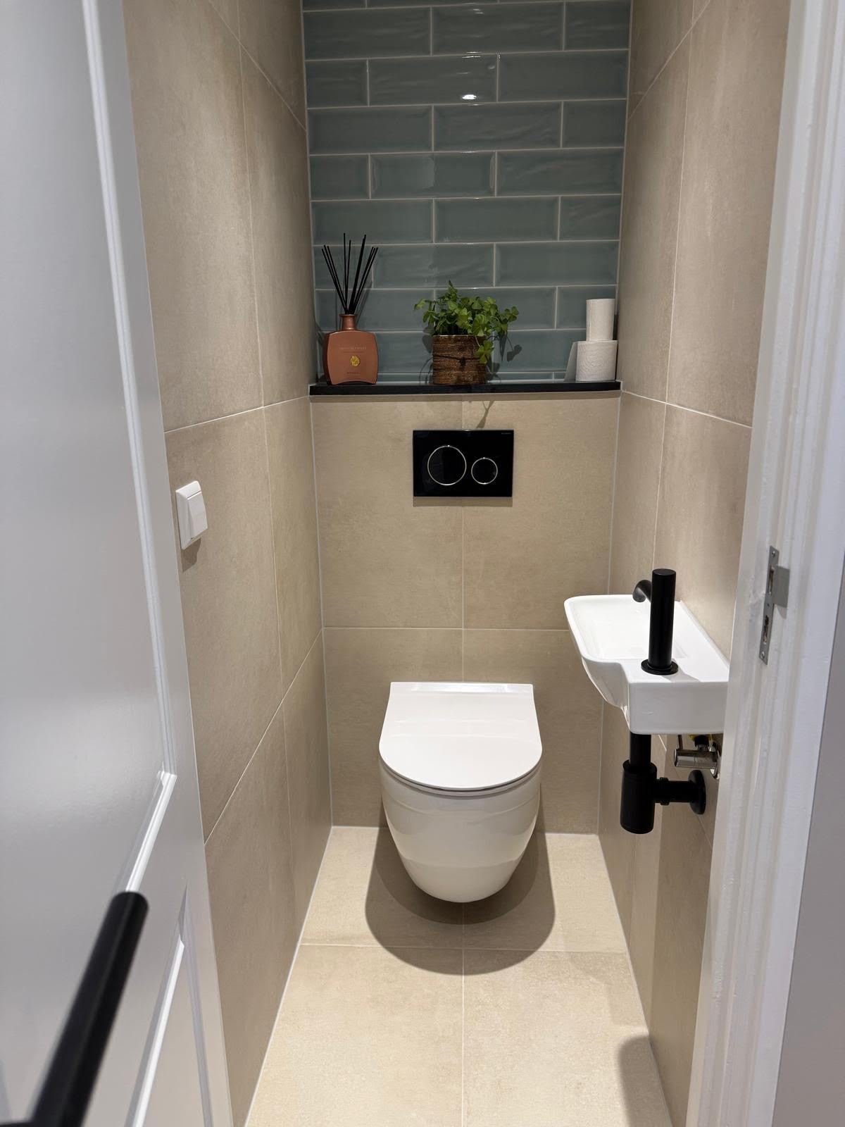 Renovated toilet with wall-hung toilet, black flush plate, green tiled niche and small hand basin
