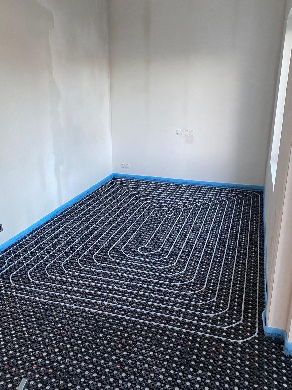 Underfloor heating pipes laid on black system panels with a blue edge strip